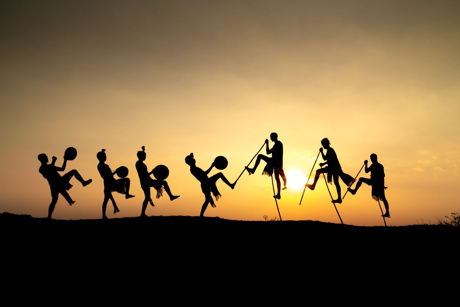 Silhouetted dancers on stilts performing against a vibrant sunset sky, exuding joy and cultural tradition.