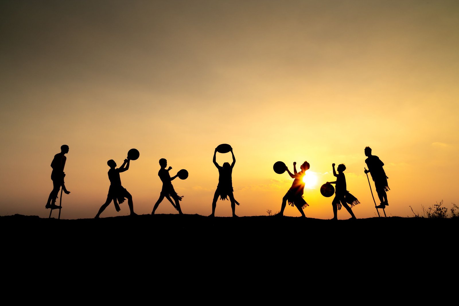 Silhouetted group of people performing with drums at sunset, creating a lively and cultural scene.