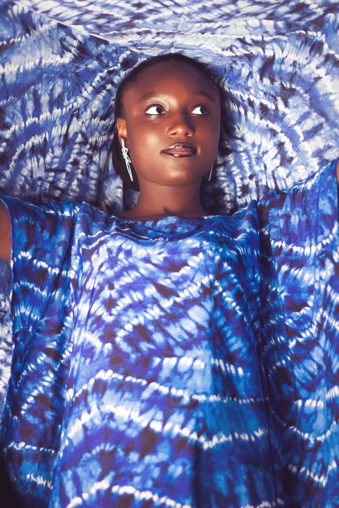 Vibrant portrait of a woman in traditional blue tie-dye fabric from Zaria, Nigeria.